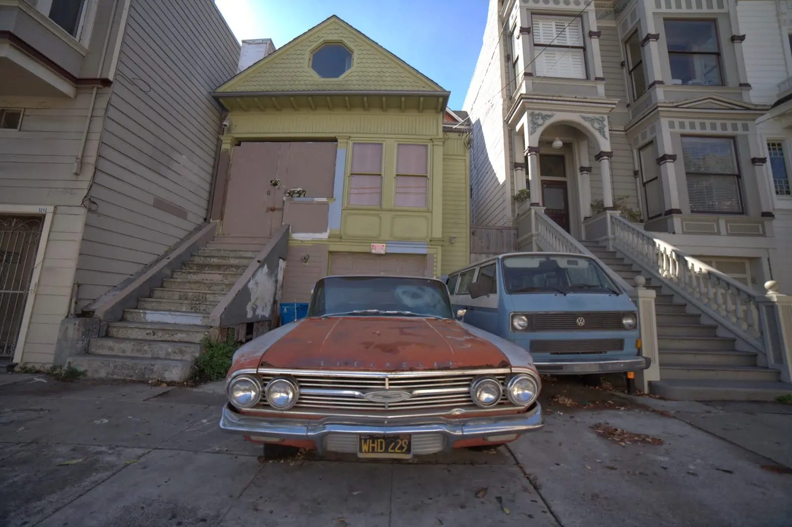 Pastel houses behind two classic cars on a sloping street