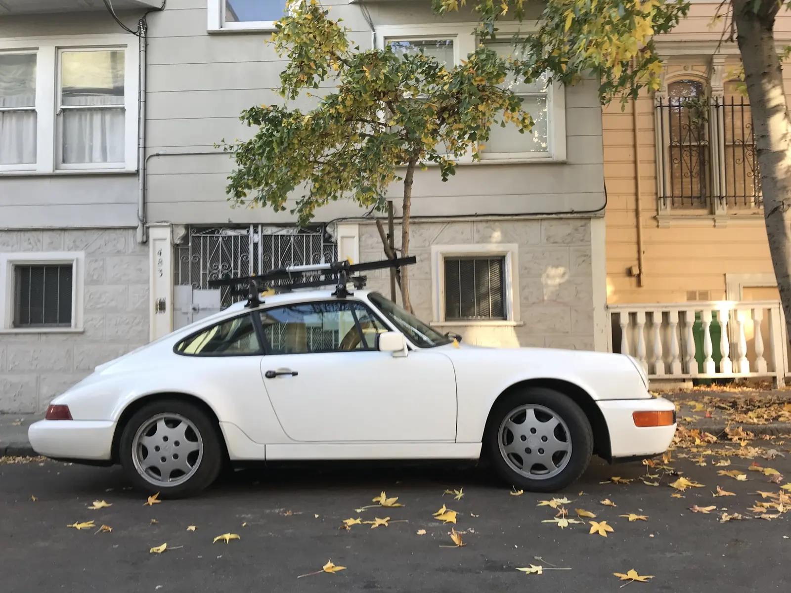 White coupe parked beside a tree and adjoining house facades
